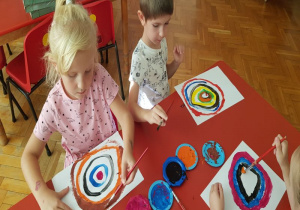 dzieci przy stoliku malują farbami koła zaczynając od kropki